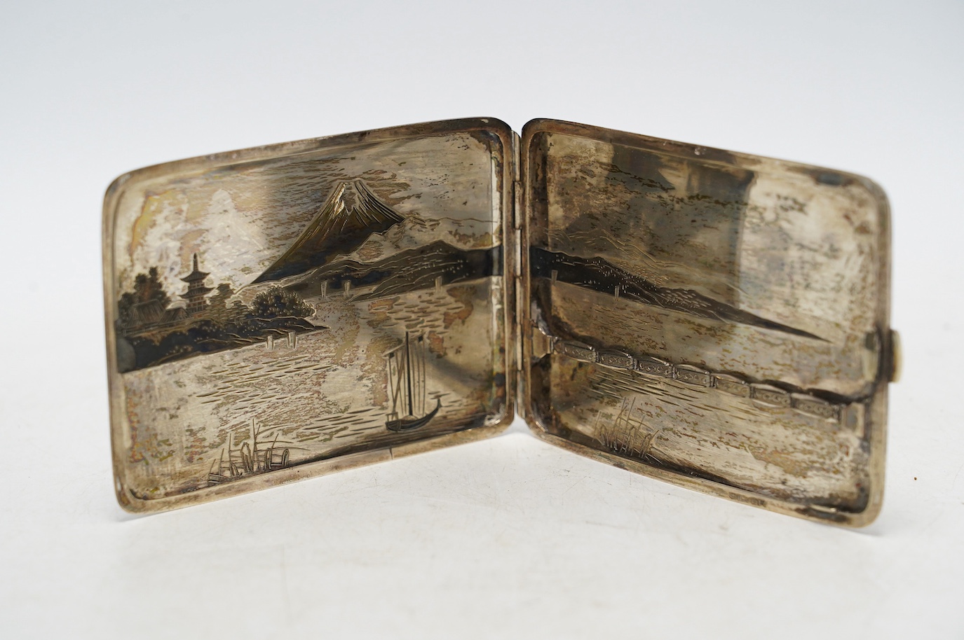 A white metal (stamped) and dark patinated Japanese silver cigarette case, decorated with a view of Mount Fuji, signed, 11cm, gross weight 113 grams. Condition - fair